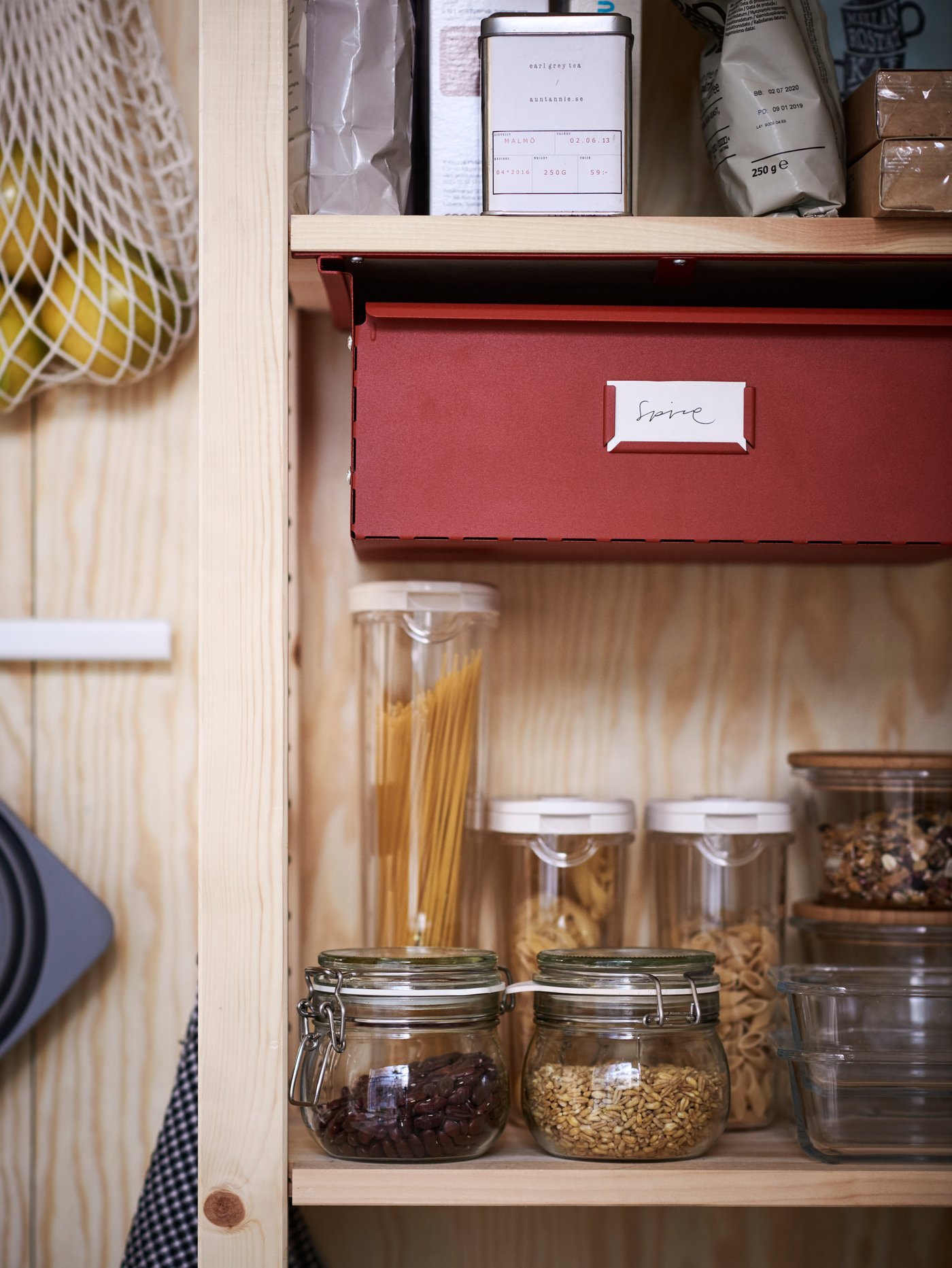 Pantry with tall wooden storage system with multiple shelves, red drawer, clear plastic and glass food jars.