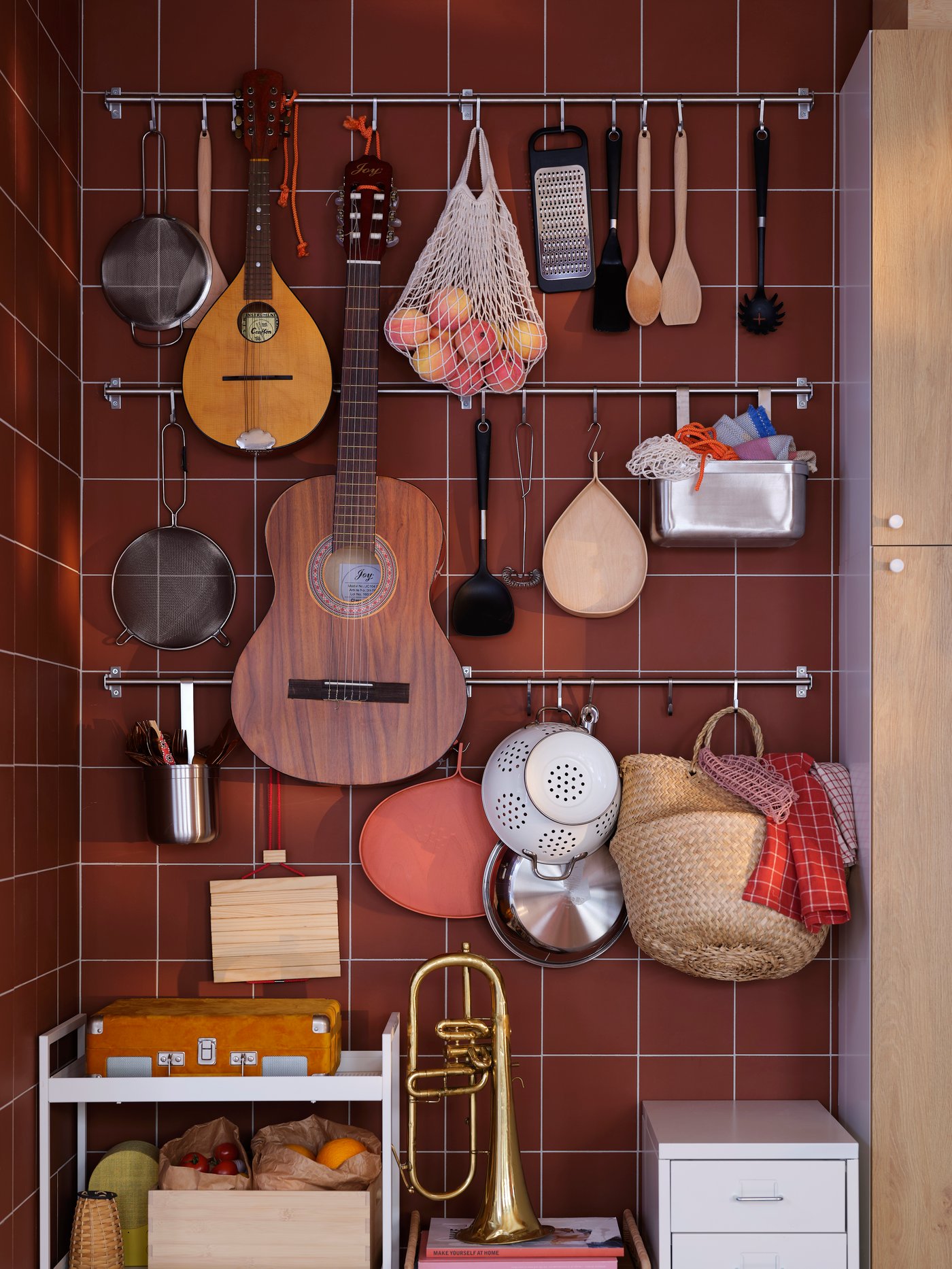 A tiled reddish-brown wall with various kitchen utensils, fruit, instruments, and other items hung on KUNGSFORS rails.