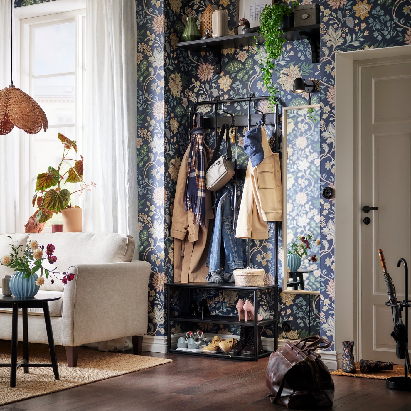 En NIPÅSEN knagerække og bænk med skoopbevaring op mod en væg beklædt med blomstret tapet og med en SKURUP lampe ved siden af.