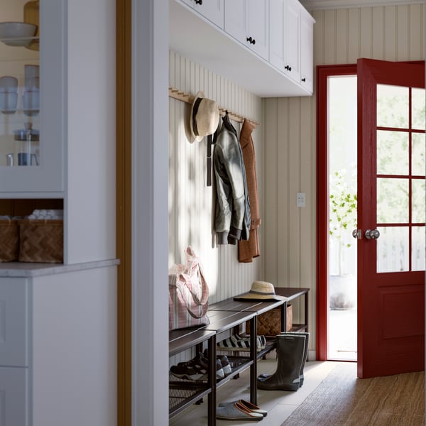 Un vestibule avec un banc brun et des crochets au-dessus pour les manteaux. Une porte rouge vif donne sur l’extérieur.