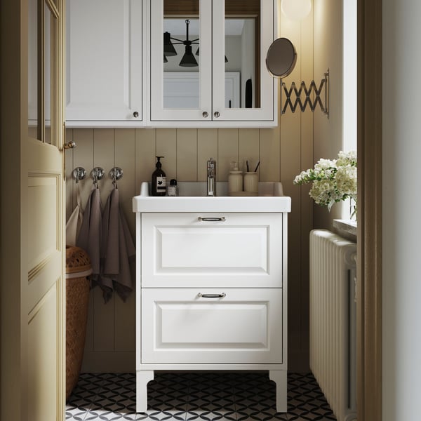 A white TÄNNFORSEN vanity with drawers and a matching mirror cabinet are placed in a bathroom with light brown walls.