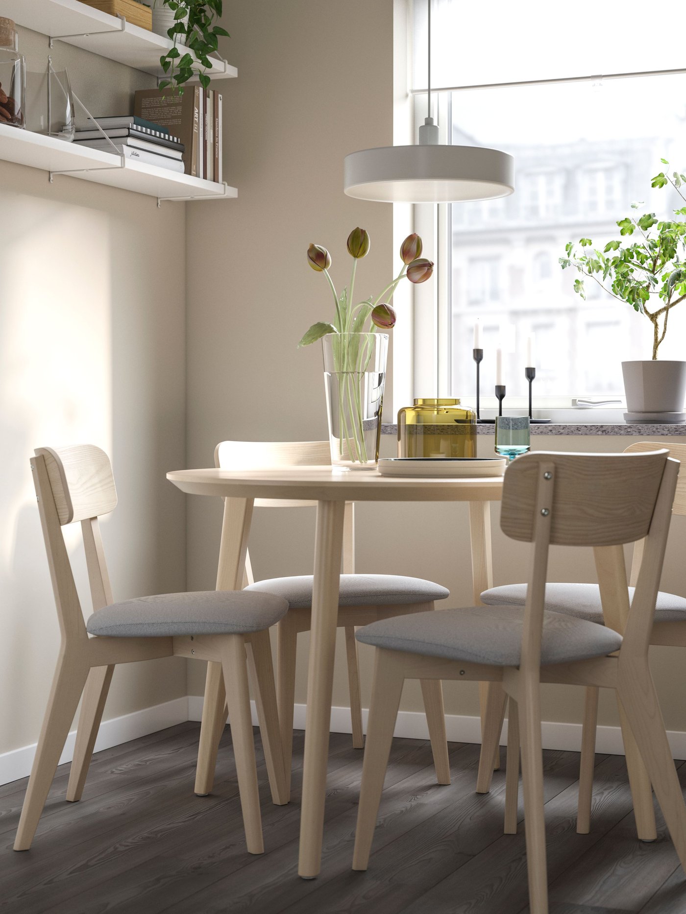 A dining area with a 4-seater dining table with four wooden dining chairs and a white/white PERSHULT wall shelf on the wall.