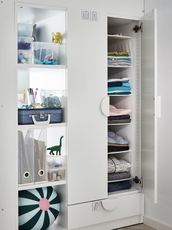 Einbaukleiderschrank seitlich des Hochbettes. Hinter den Türen sind gefaltete Kleidung und Boxen mit Gegenständen auf den Böden zu sehen.