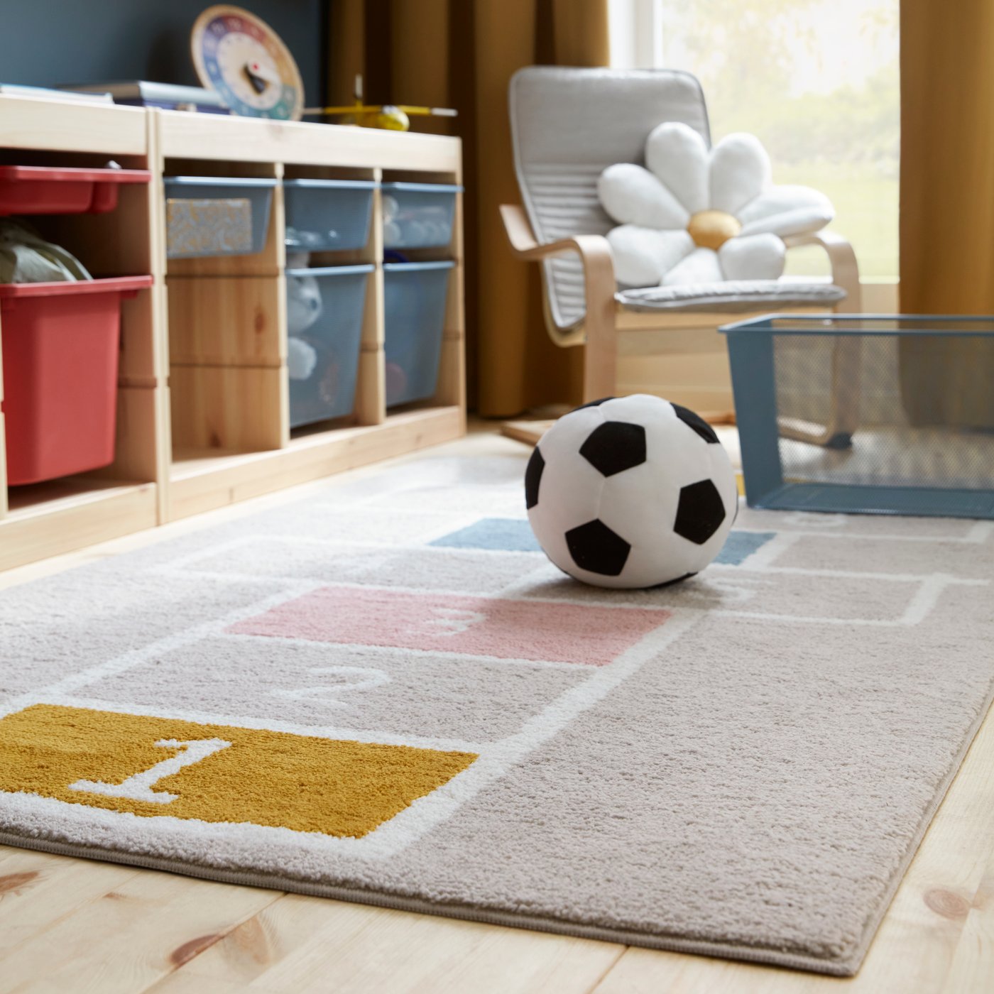 En matta från STÄPPSPARV med mönster placerad i ett rum med en fotboll i textil och förvaringsenheter i nät.