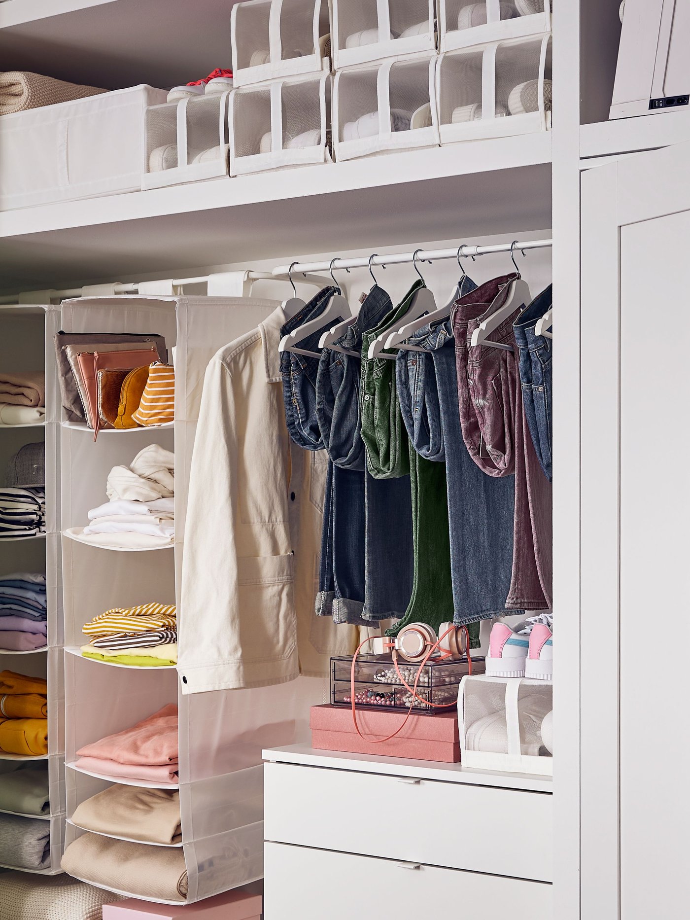 A white wardrobe with clothes hanging on shelves where there is another type of storage.
