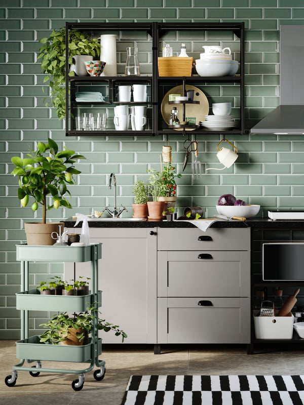 Dapur ENHET yang mempunyai bahagian hadapan berwarna kelabu dan rangka berwarna antrasit/kelabu bersandar pada dinding berjubin berwarna hijau dan troli yang berisi tumbuh-tumbuhan.