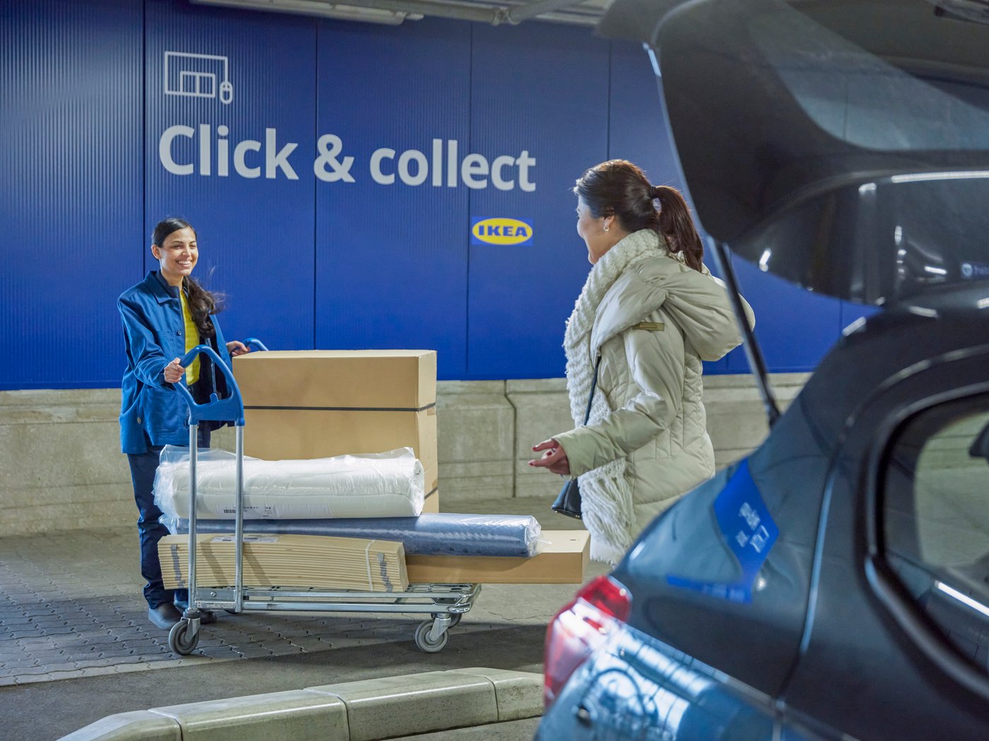 Ženska prevzema nakupljeno blago s storitvijo Klikni in prevzemi, predaja ji ga zaposlena v podjetju IKEA.