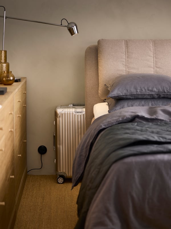 Twee TONSTAD ladekasten met 6 lades van eiken fineer staan tegenover een LILLFJÄLLET gestoffeerd bed met een koffer achter het hoofdbord.