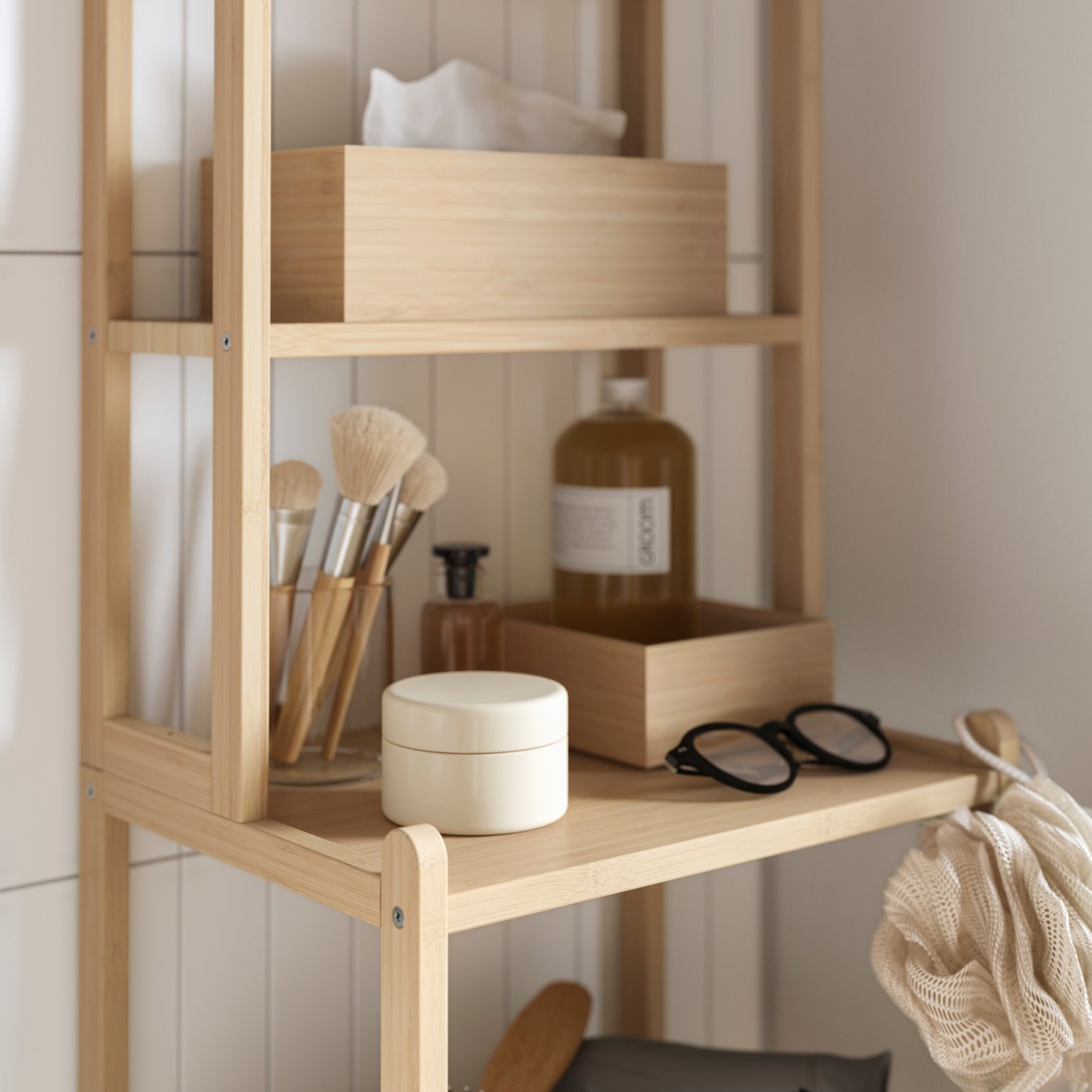 STEGESUND shelf unit in light bamboo with storage boxes, make-up brushes, bottles and glasses arranged on open bathroom shelves.
