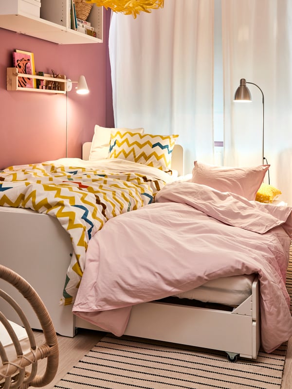 A woman sitting on two stacked UTÅKER pine beds reading a magazine, a white side table, a multicolour rug and a pendant.