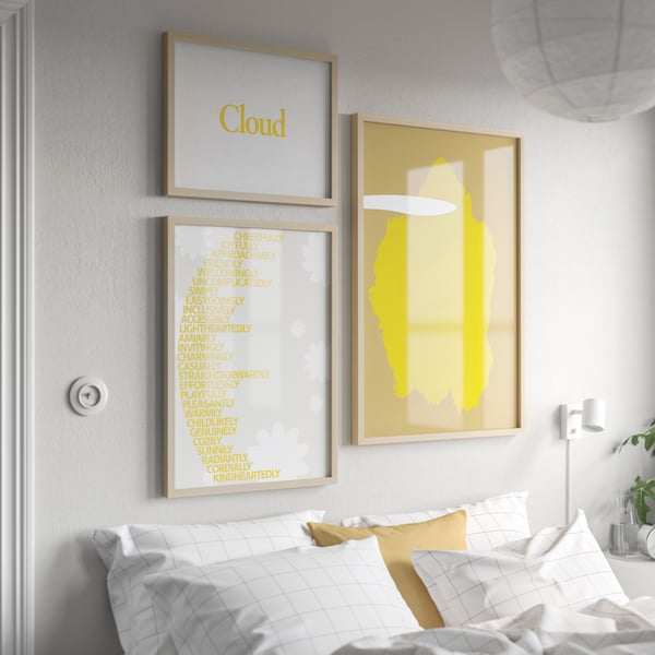 An der Wand über einem Bett mit Bettzeug in weisser Bettwäsche hängen drei verschieden grosse RÖDALM Rahmen in Birkenachbildung. In jedem ist ein modernes Kunstwerk in Gelb zu sehen.