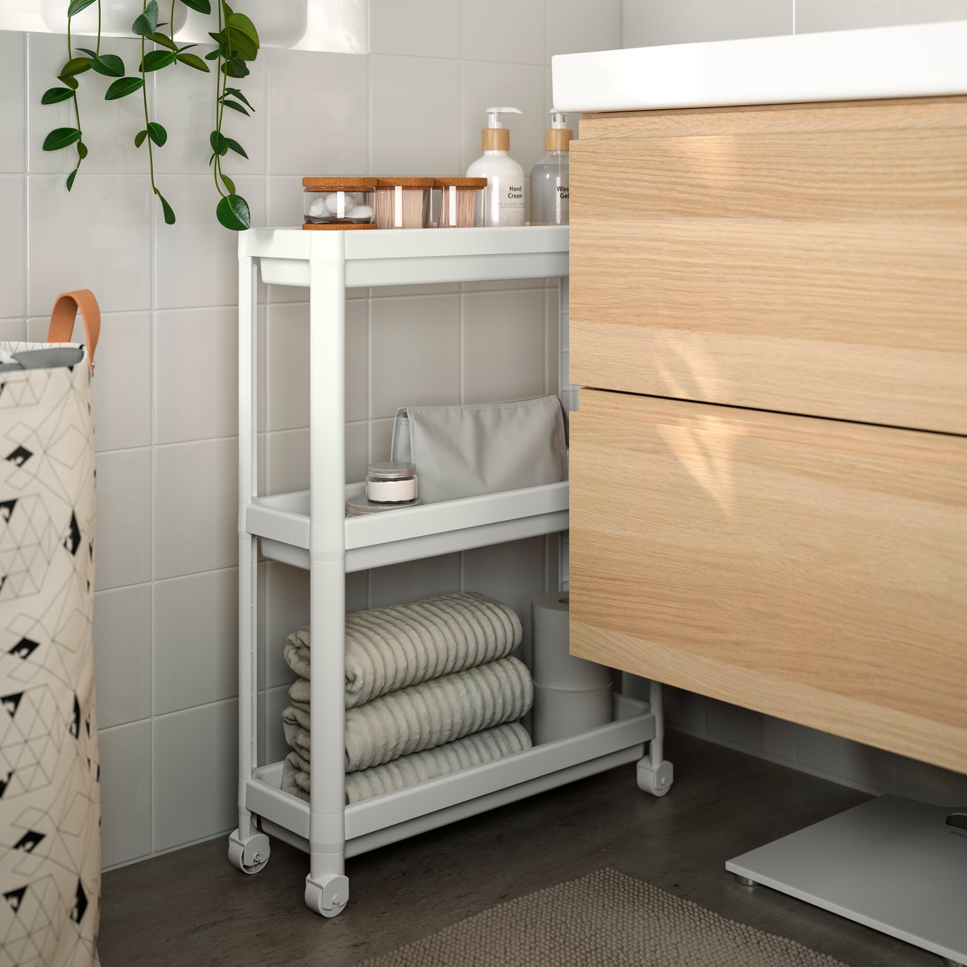 Un baño con mueble de lavamanos donde se aprecia un carrito de baño delgado inserto en el espacio lateral entre el mueble y la pared.