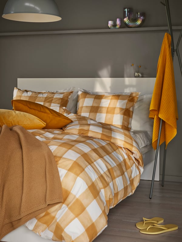 The cover-meets-pillow part of a bed neatly made with KANTNEPETA bed linen, a pair of dark-turmeric cushions mixed in.