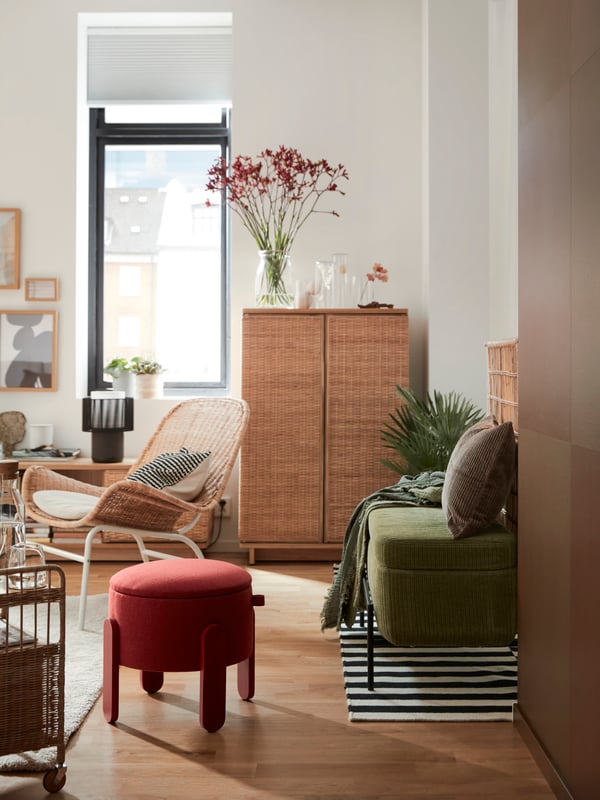 Es ist ein Wohnzimmer mit einem roten FÖRLUNDA Bodenkissen, einer VALTORP Bank und einem FRYKSÅS Schrank, Polstersessel und Aufbewahrungselement mit Rollen zu sehen.