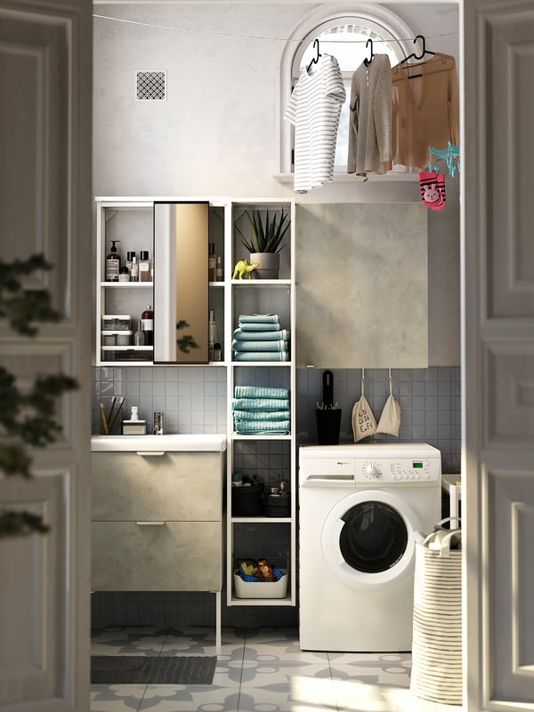 A white and grey washbasin, white ENHET open and closed shelves, a washing machine and shirts drying on a laundry line.