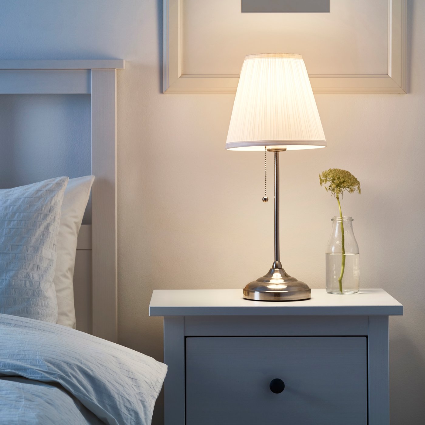 A nickel-plated/white ÅRSTID table lamp in the bedroom