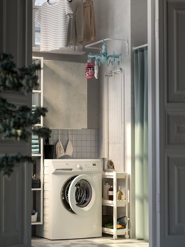 The laundry nook showing a washing machine, a grey cabinet with door, a white narrow trolley, a clothes bar hung on the wall.