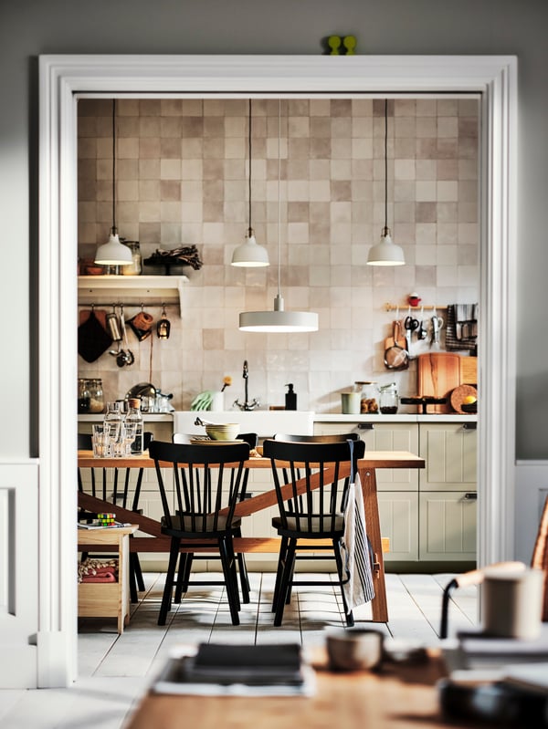 A kitchen with beige STENSUND drawer fronts and an oak MÖCKELBY table surrounded by black NORRARYD chairs.