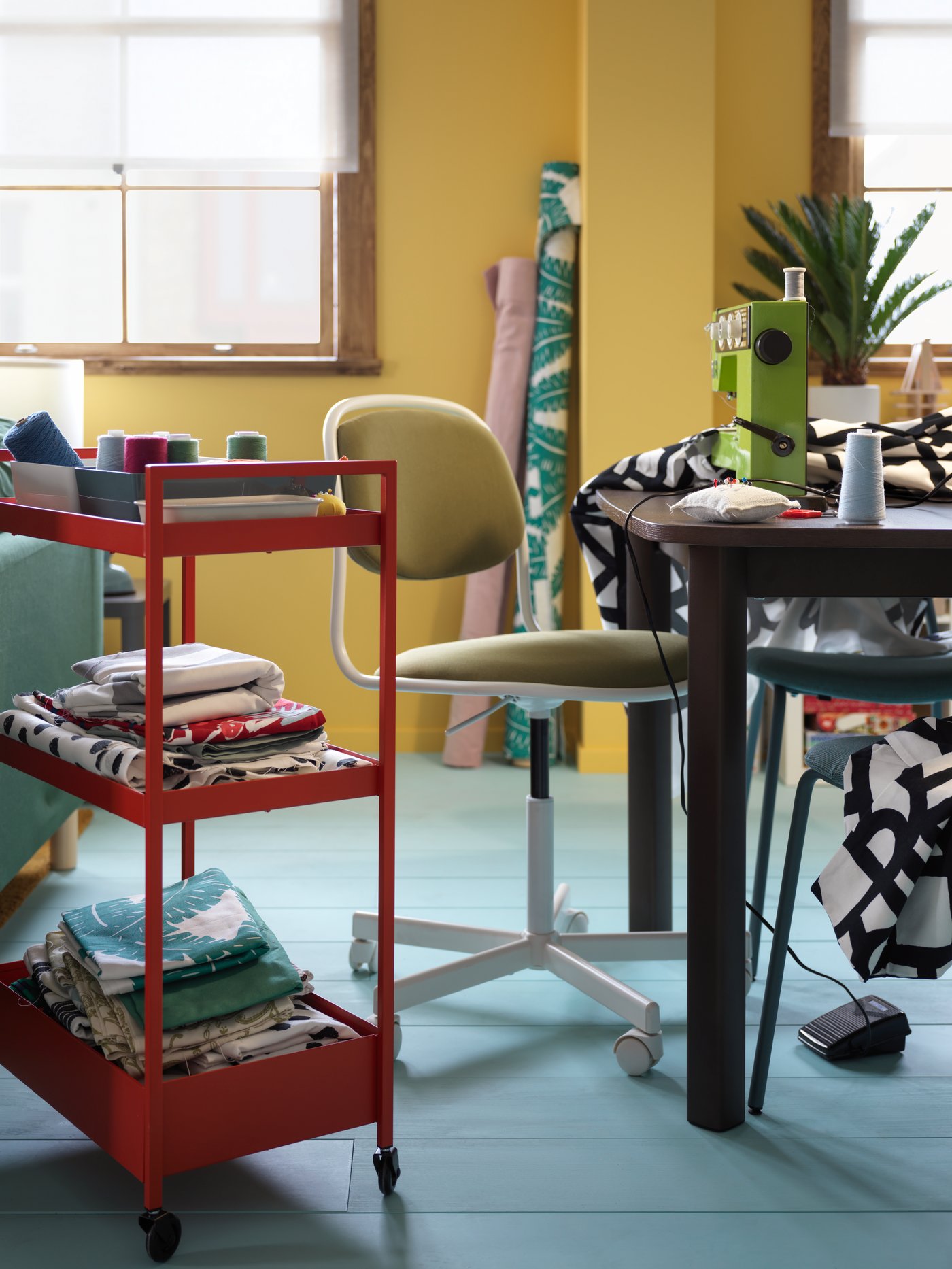 A white and yellow-green ÖRFJÄLL swivel chair in-between a table and a red NISSAFORS trolley filled with assorted fabric.