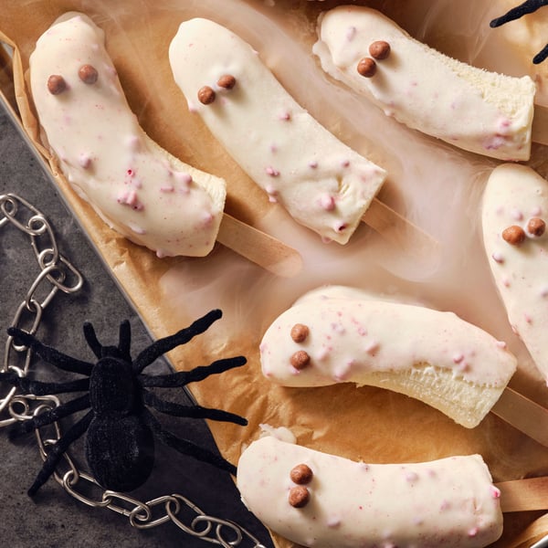 Frosty banana ghost popsicles doppade i BELÖNING vit choklad med hallon, med en leksaksspindel och kedja på sidan.