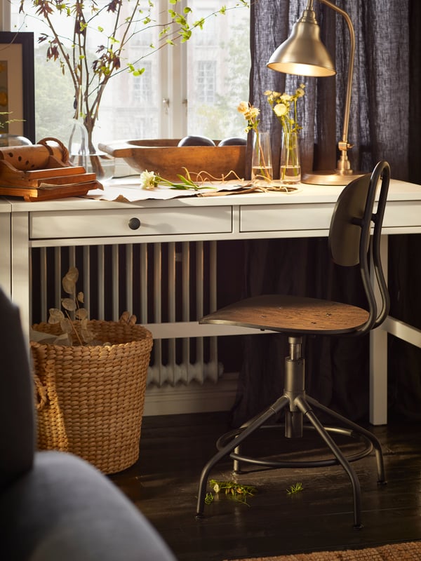 Un bureau HEMNES à deux tiroirs sur lequel se trouvent une lampe de travail en effet étain et une chaise pivotante KULLABERG noire.