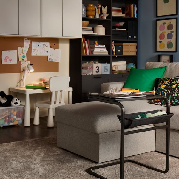 Un sofá cama BÅRSLÖV de 3 plazas, beige y gris, con chaise longue, en una sala de estar luminosa, rodeado por una zona de juegos infantil.