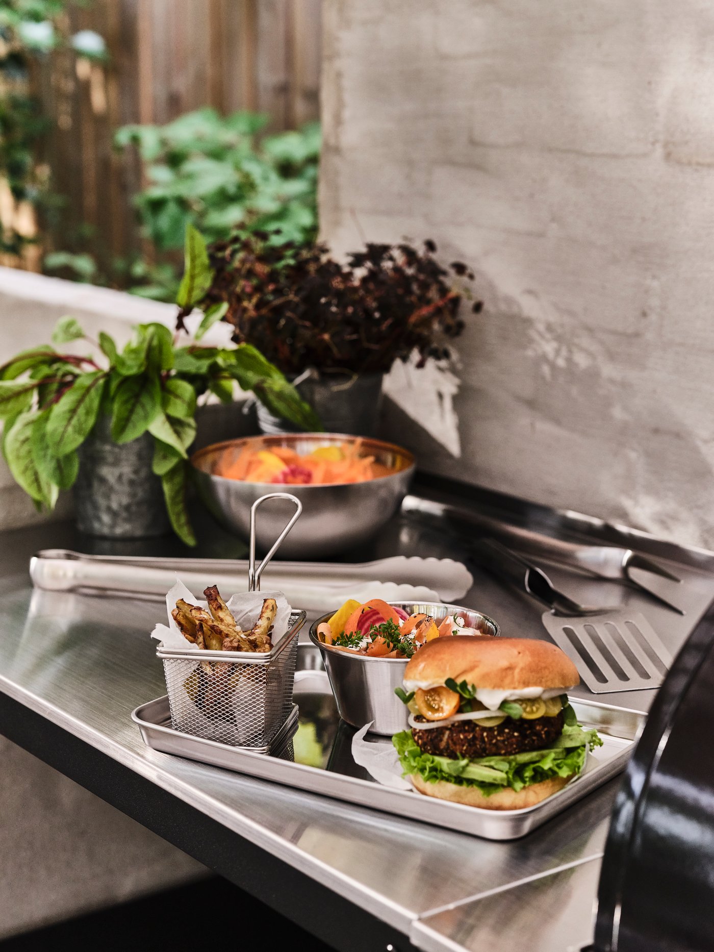 A GRILLTIDER serving basket, serving bowl and barbecue tool set prepared with a hamburger meal on an outdoor worktop.