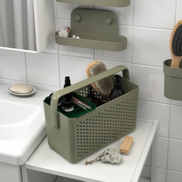 Un estante de pared ÖBONÄS verde grisáceo con ventosa colgada en la pared de un baño y un canasto UPPRÄMEN con cepillos y artículos en el interior.