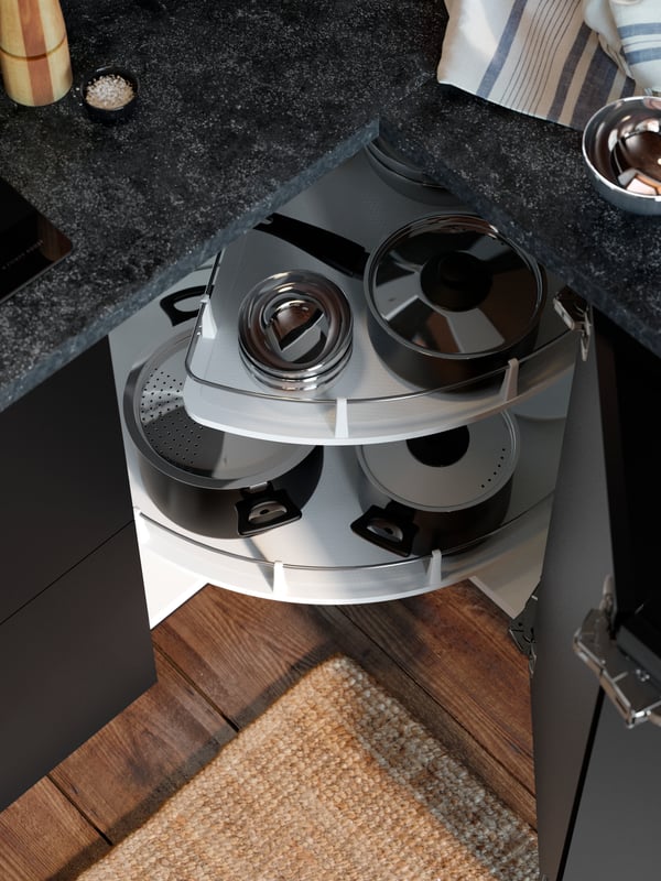 A cabinet door is open revealing a UTRUSTA corner base cabinet carousel with pots and stainless steel bowls.