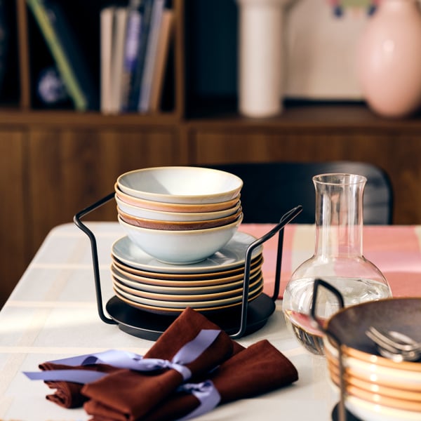 A table set with FÄRGKLAR bowls and plates stacked on top of each other on an organiser, some napkins neatly folded.