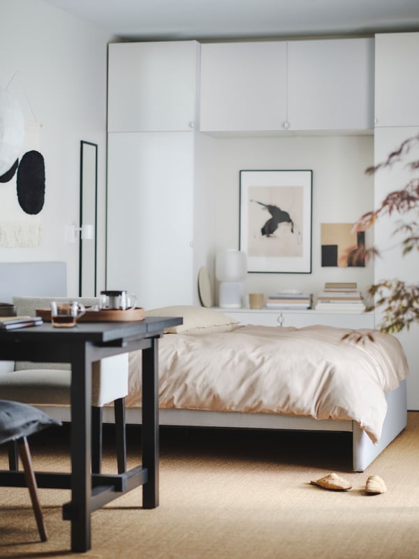 Blick in ein helles Wohn-Schlafzimmer mit gemütlicher beiger Bettwäsche aus unserer LUKTJASMIN Serie.