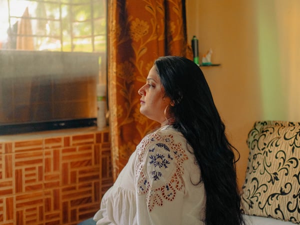 Lady sitting on her bed looking reflectively out of her window.