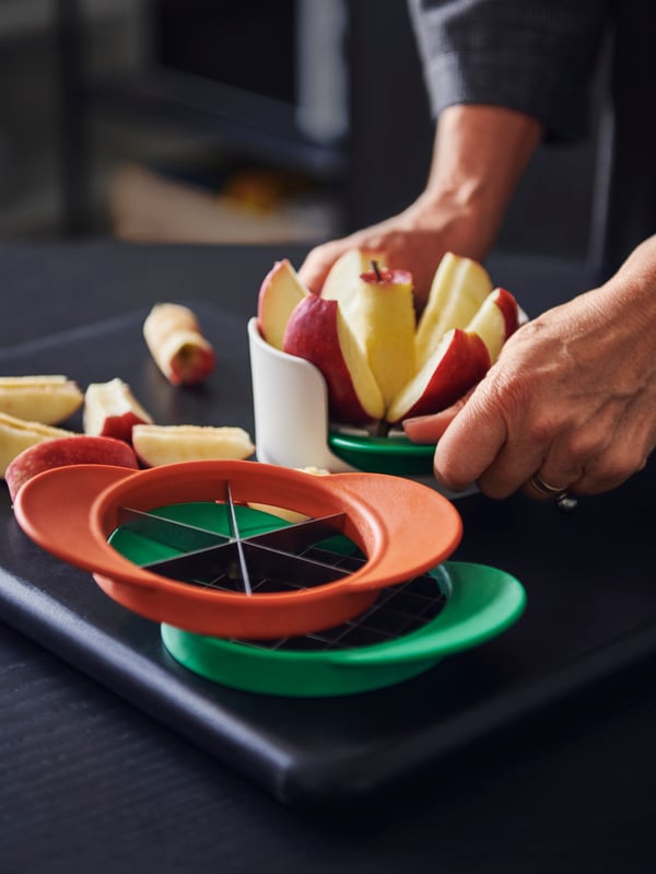 Some UPPFYLLD fruit cutters in a set of four in mixed colours, a person’s hands cutting an apple with the fruit cutter.