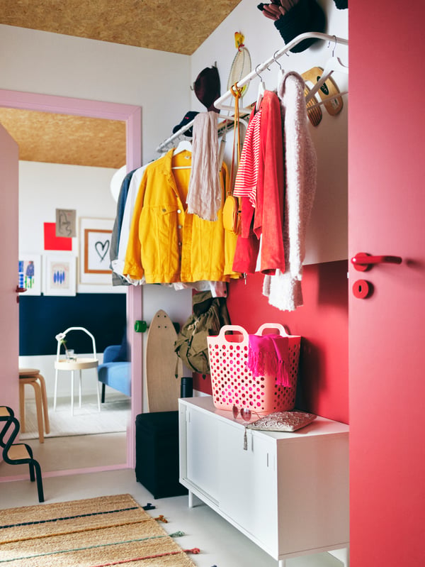 A colorful hallway with garments on white MULIG clothes bars on the wall above a red NIKKEBY chest of drawers.