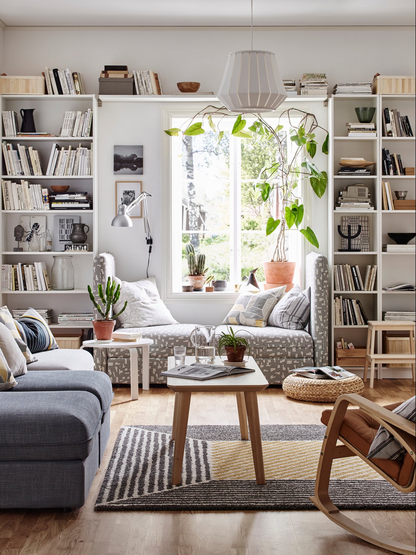 Es ist ein helles Wohnzimmer mit weissen Wänden und zwei BILLY Bücherregalen in Weiss rechts und links des Fensters zu sehen.