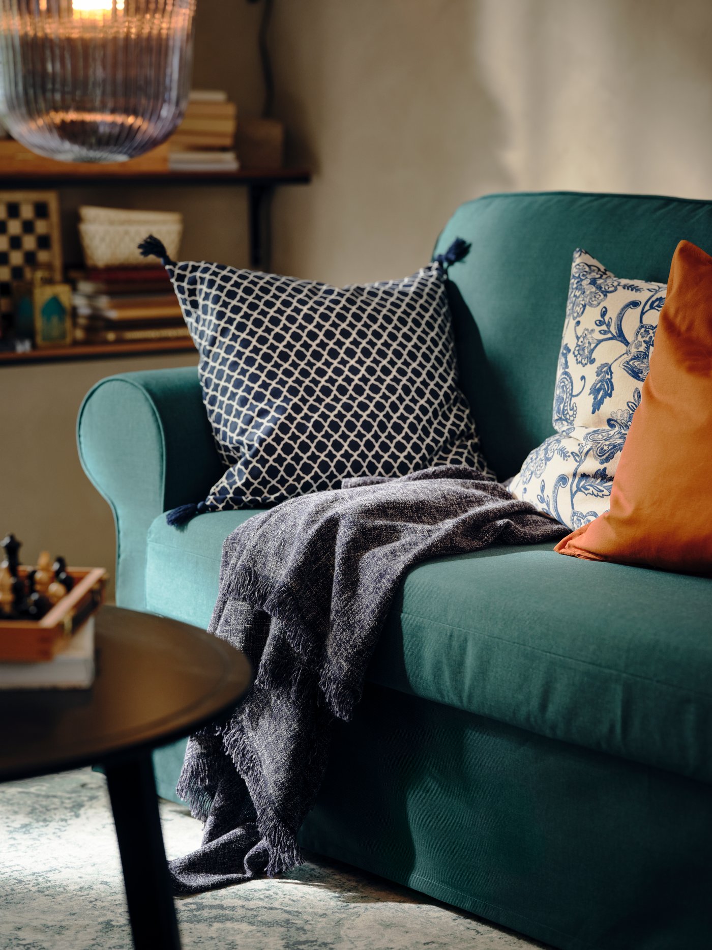 Des coussins et un plaid sur un convertible VRETSTORP turquoise foncé, à côté d’une table basse KRAGSTA noire.