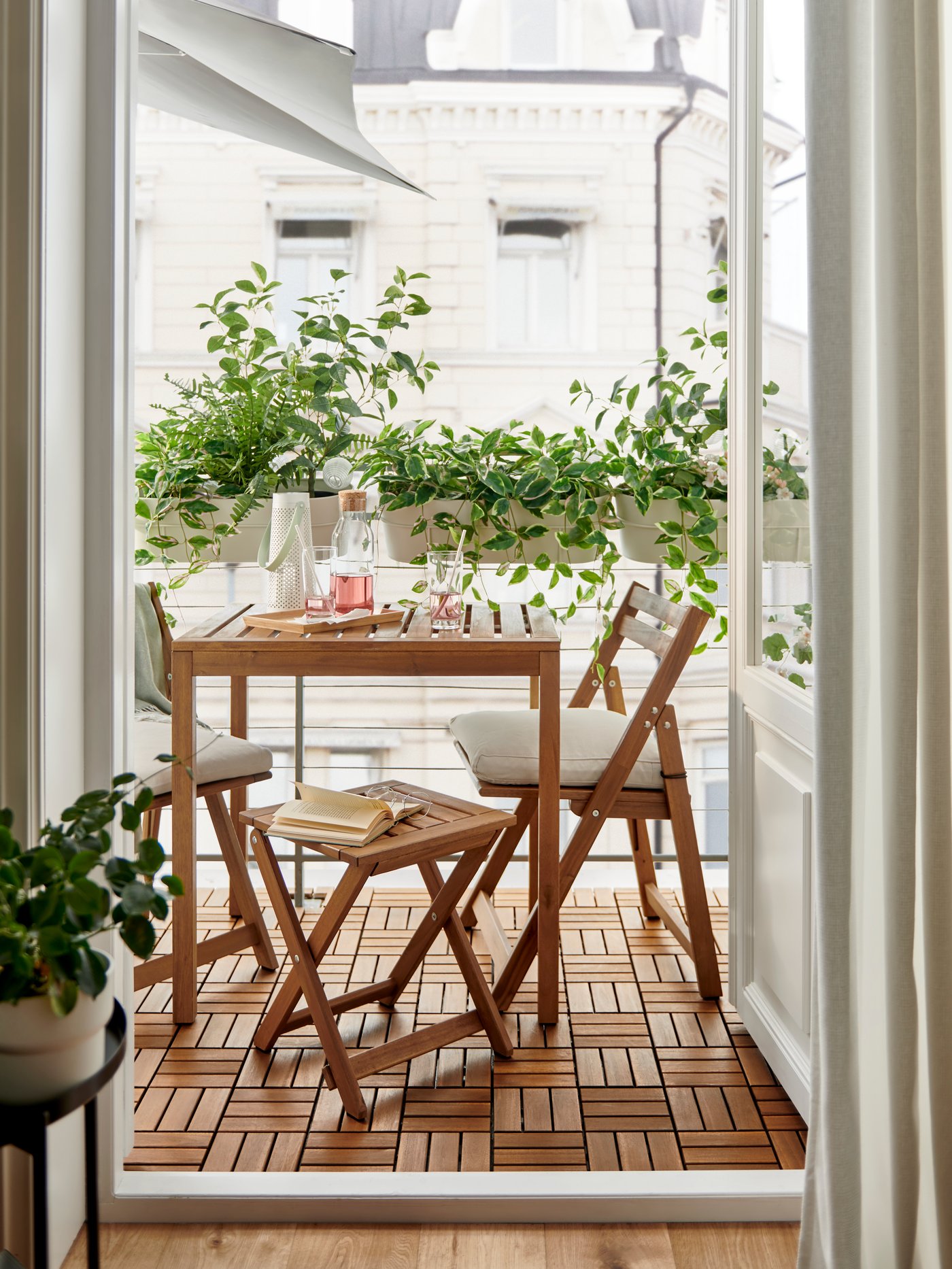Balkon mit zwei Holzklappstühlen und einem Tisch aus der NÄMMARÖ Serie. Darüber hinaus sind verschiedene Grünpflanzen zu sehen.