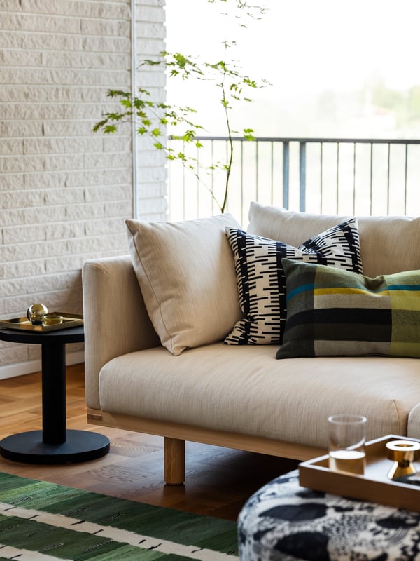 Cushions resting on a beige STOCKHOLM 2025 3-seat sofa, a black side table beside it, and greenery in the background.