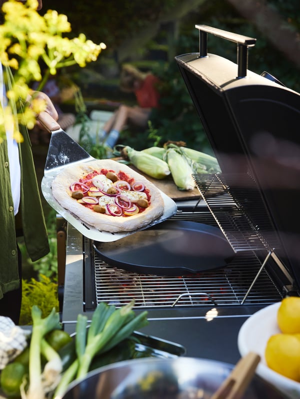 Spremanje domaće pice na BÅTSKÄR roštilju u bašti pomoću GRILLTIDER lopatice i pleha za picu radi savršene teksture.