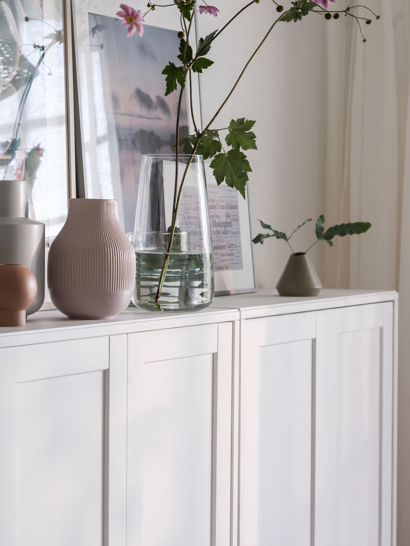 Part of a white HAVSTA cabinet with plinth, with various objects including vases and works of art on it, against a wall.