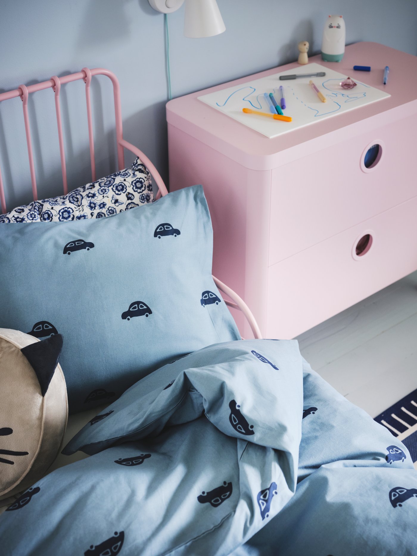Textil infantil BARNDRÖM celeste con autos azul oscuro junto a velador rosado BUSUNGE.