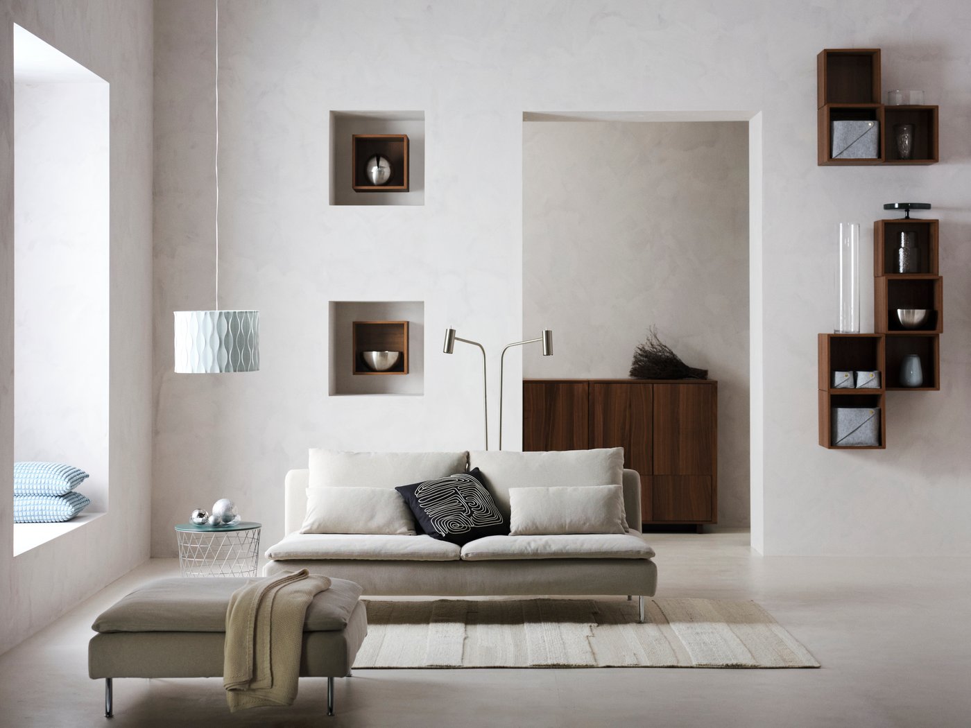 Ein minimalistisches Wohnzimmer in warmen Grautönen mit einem hellgrauen SÖDERHAMN Sofa und EKET Wandregalen in Würfelform und dunklem Holzton