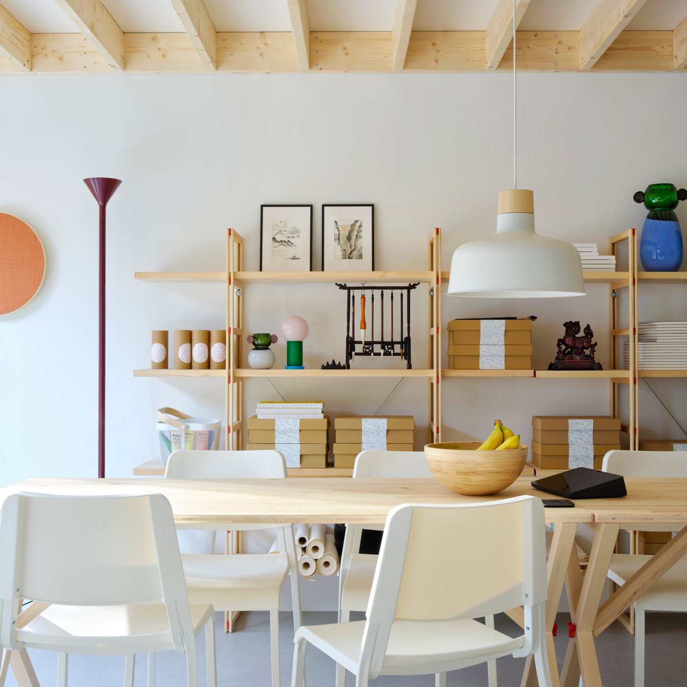 Meeting room/workspace with open display shelves on back wall. Foreground shows natural wood table and white chairs.