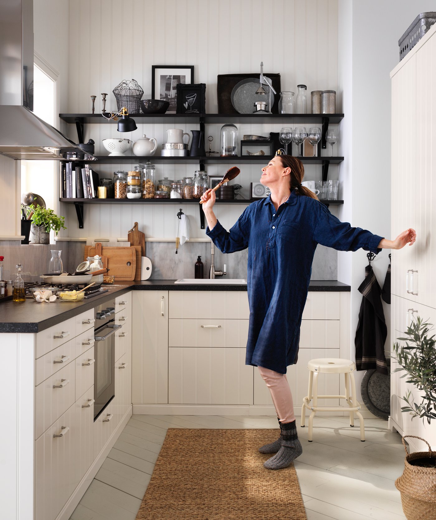 Une femme danse et chante au milieu d’une cuisine en forme de L avec des armoires blanches et des comptoirs noirs