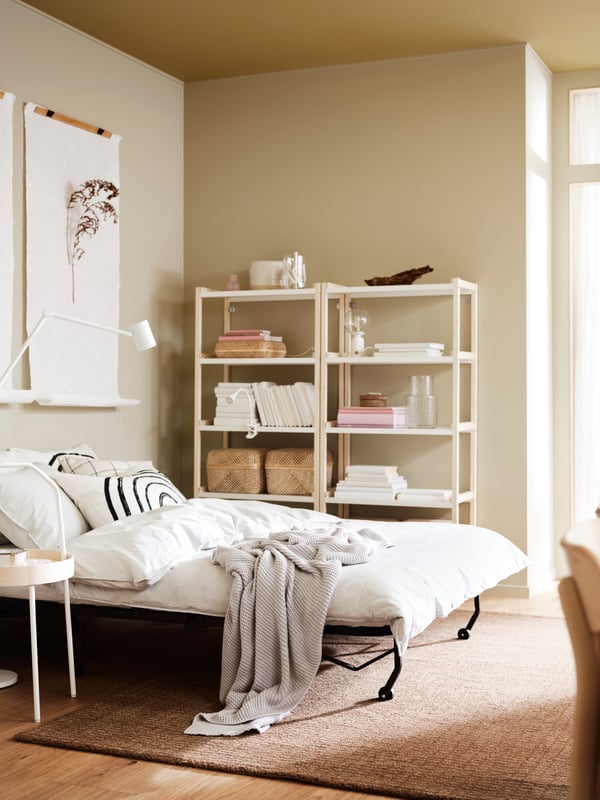 A light room with a folded-out LYCKSELE LÖVÅS two-seat sofa-bed placed next to two EKENABBEN shelving units.