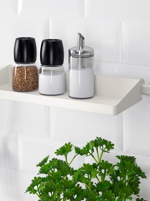 שתי מטחנות תבלינים IKEA 365+ IHÄRDIG וכלי לסוכר עם חלוקה למנות DOLD ניצבים על מדף SUNNERSTA מעל עציץ עם פטרוזיליה.