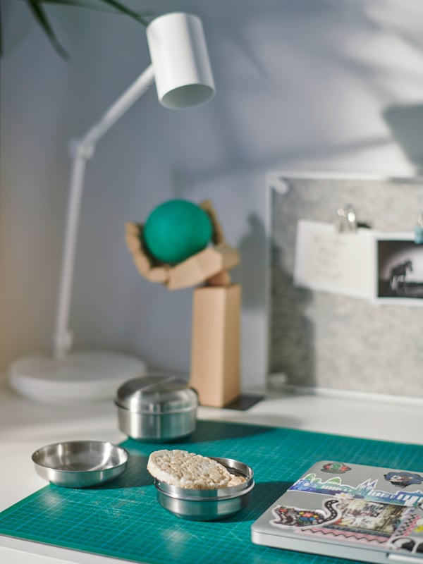 Galletta di riso in un contenitore per snack LÄTTUGGAD aperto. Il contenitore si trova su una scrivania accanto a un computer portatile - IKEA.