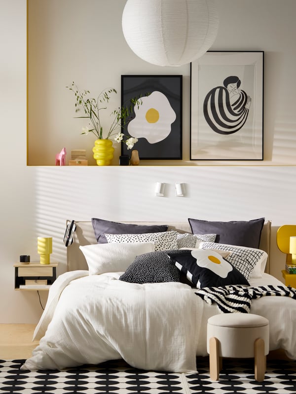 Un dormitorio con ropa de cama IKEA y sobre la cama láminas decorativas enmarcadas.