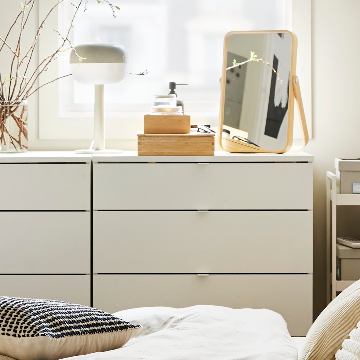 Recámara con dos cómodas VIHALS blancas de 4 cajones, con objetos decorativos y una lámpara de mesa, junto a una ventana grande.