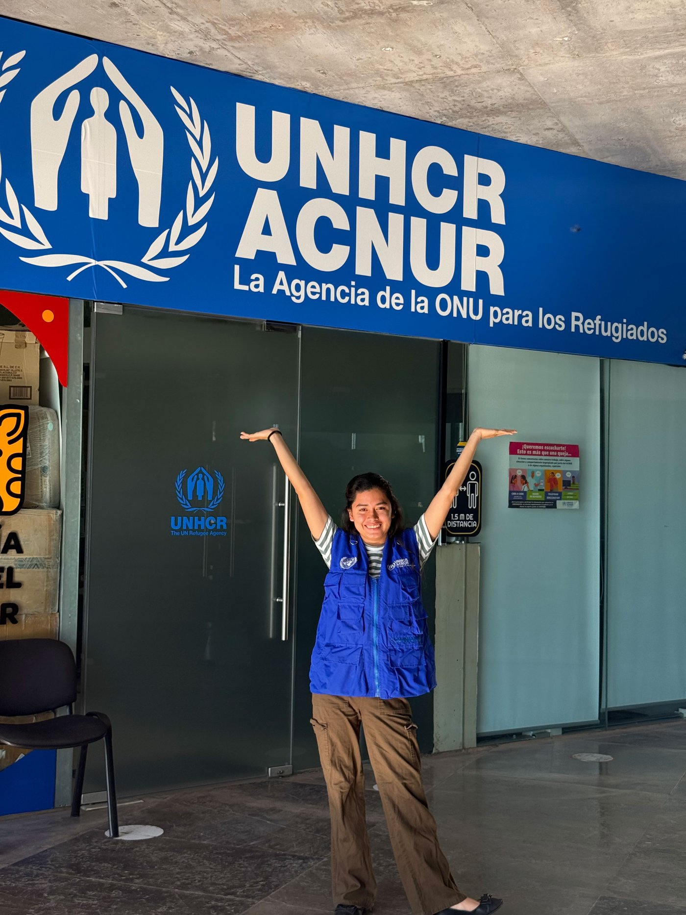 Natalie steht vor einem UNHCR-Büro und lächelt mit erhobenen Armen.